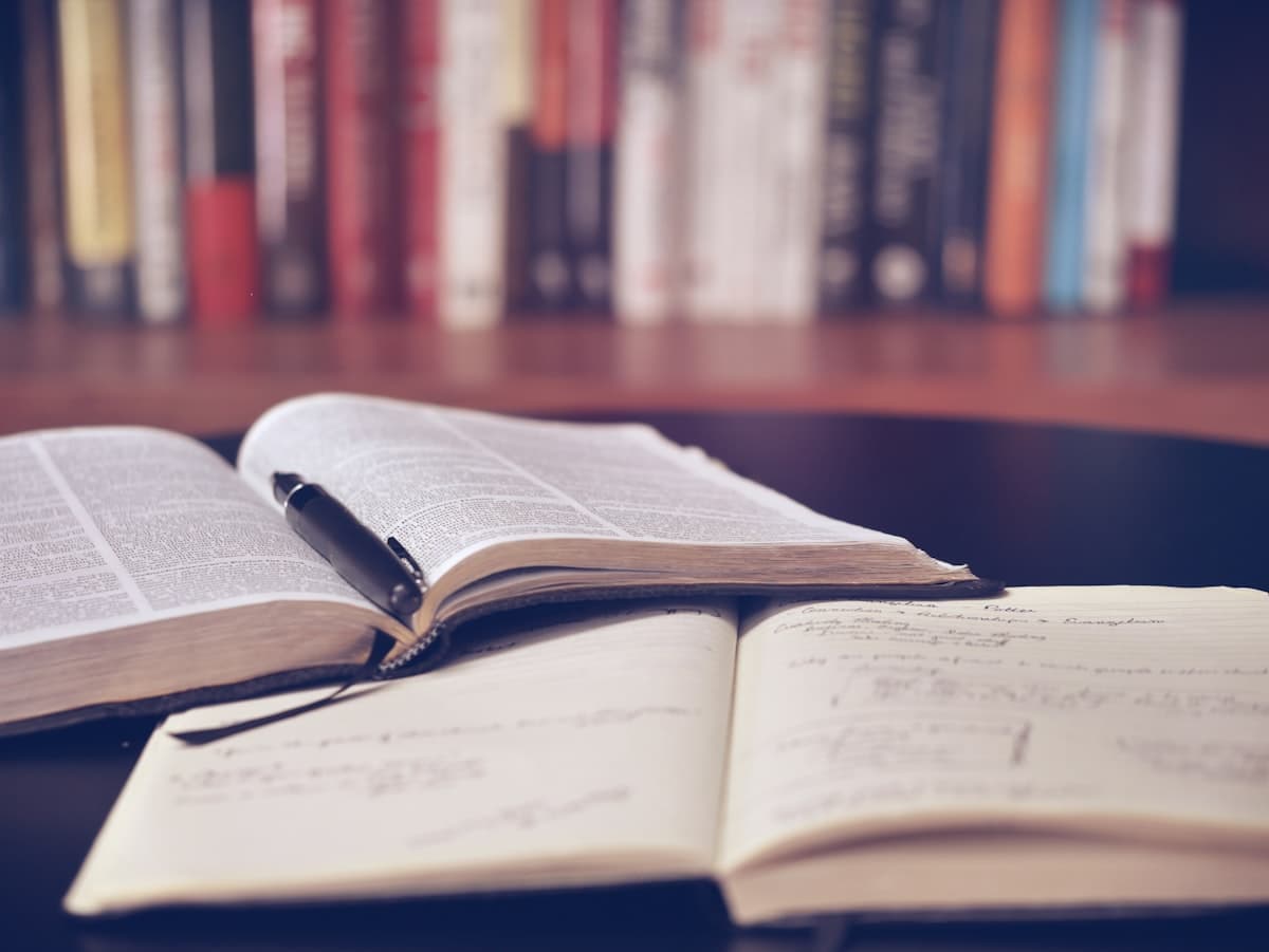 An open reference book and handwritten notebook with a pen, representing the basics of learning how to invest